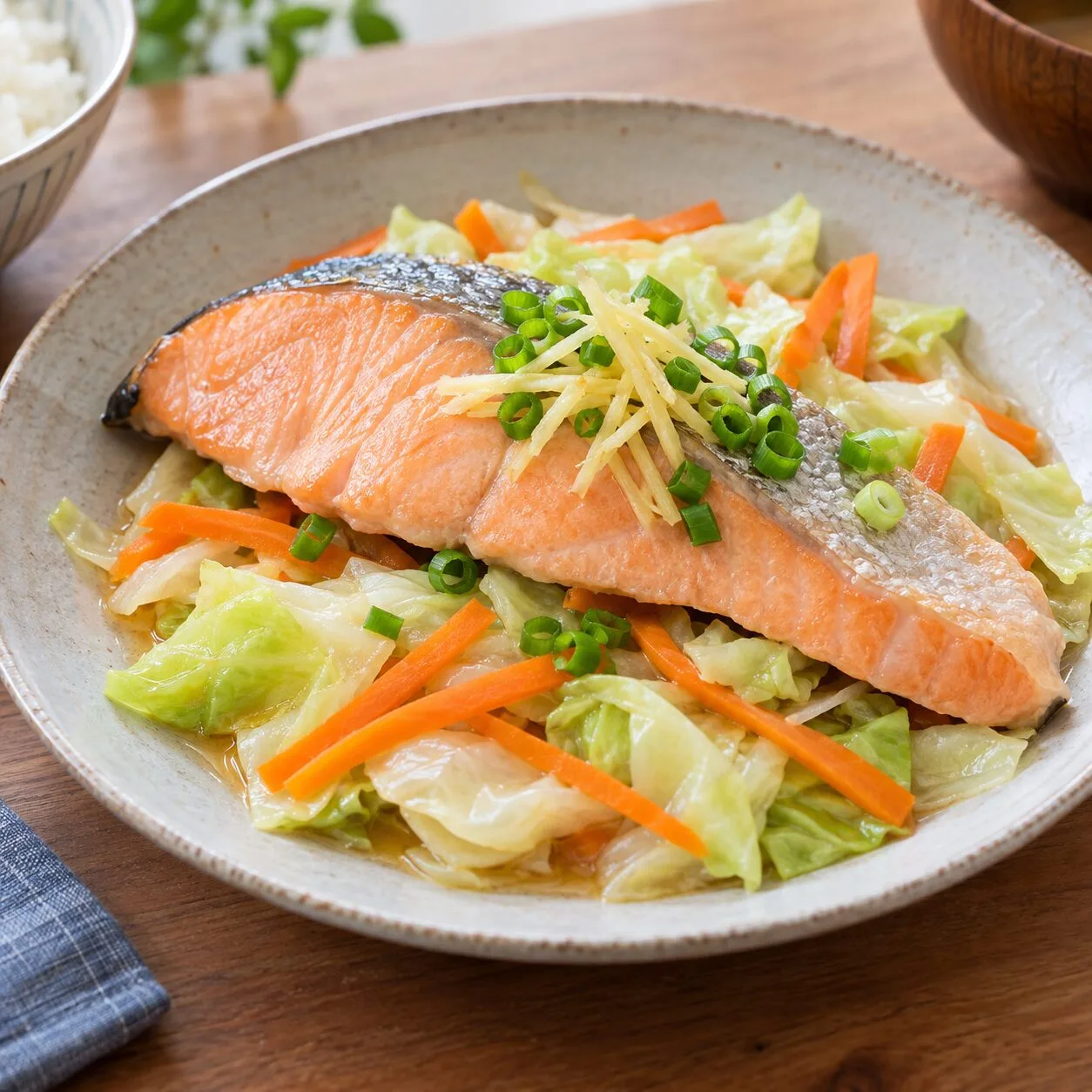 蒸したキャベツとにんじんの上に鮭を盛り、細切りしょうがと小ねぎを添えた料理